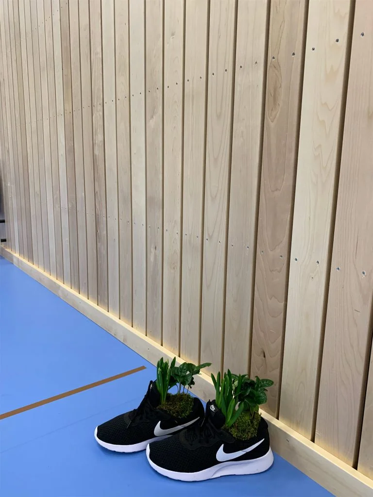 En idrottshall med träpanel-väggar. Ett par skor med plantor i syns på golvet.
