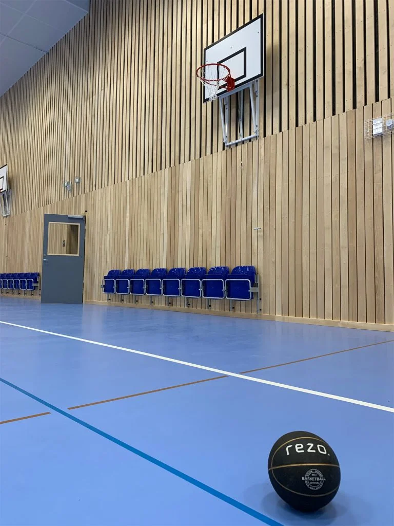 En idrottshall med träpanel-väggar. En svart basketboll syns på golvet.