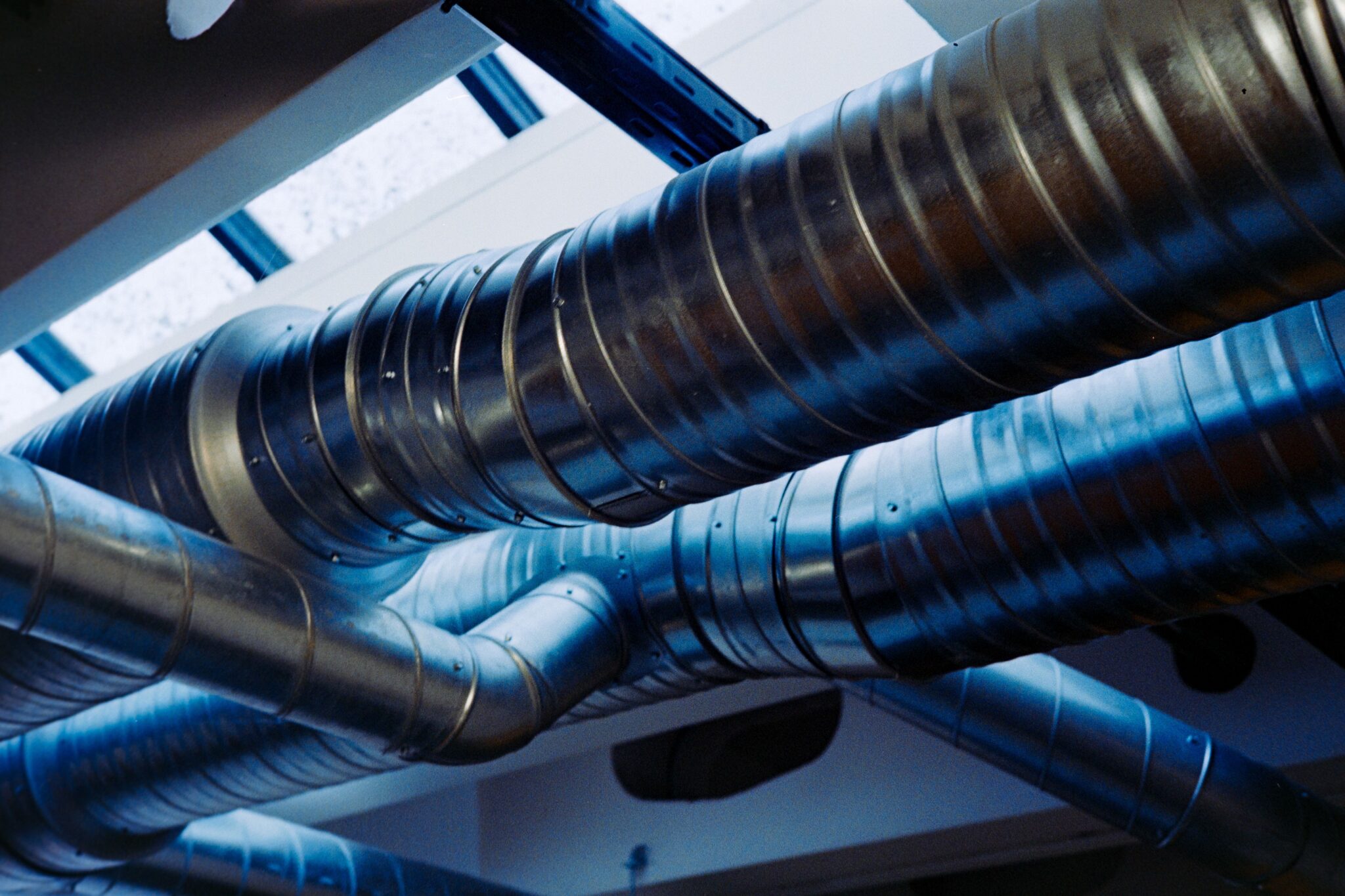 Grova, korrugerade ventilationsrör i metall som löper kors och tvärs under taket i en byggnad.