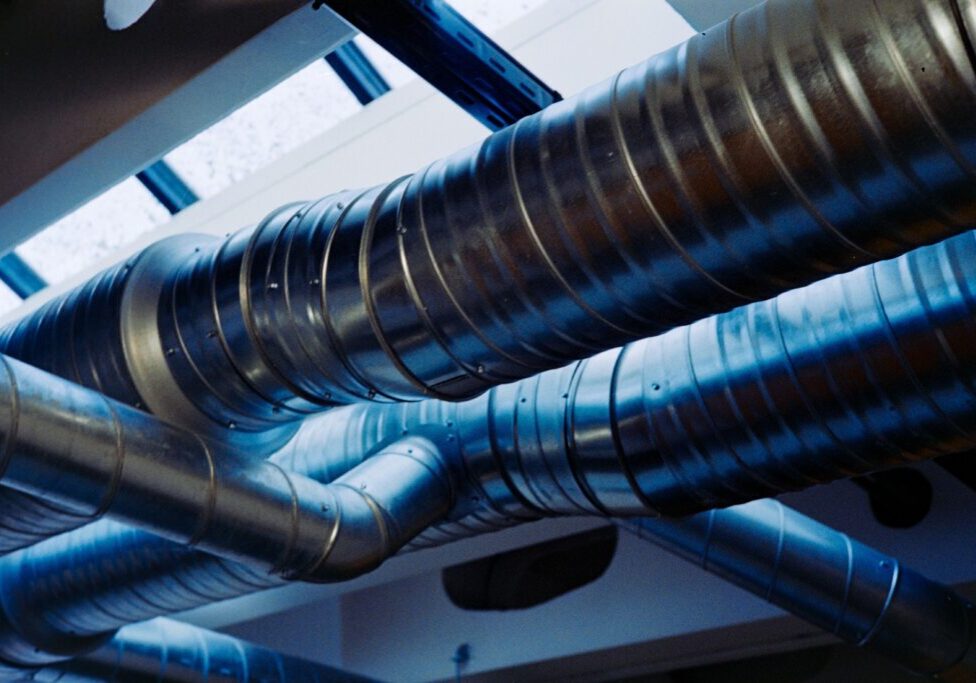 Grova, korrugerade ventilationsrör i metall som löper kors och tvärs under taket i en byggnad.