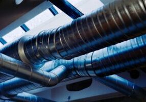 Grova, korrugerade ventilationsrör i metall som löper kors och tvärs under taket i en byggnad.